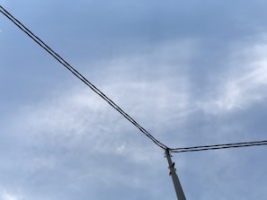 An overhead view of a utility pole with wires extending across a cloudy sky, indicating a network of power or communication lines.