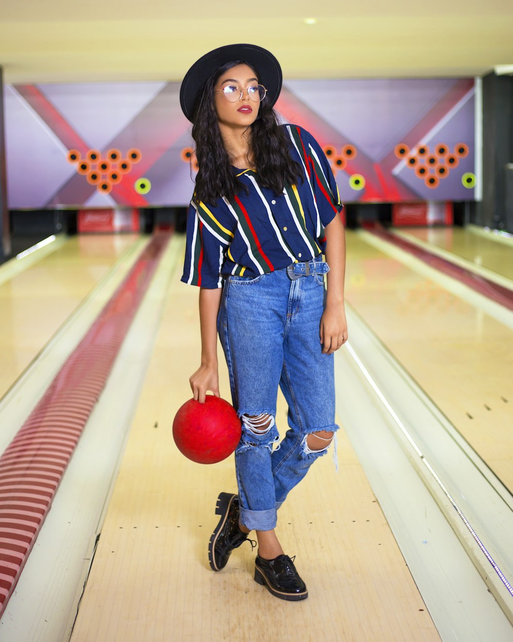 woman in blue denim jeans and black white and red striped shirt standing on brown wooden