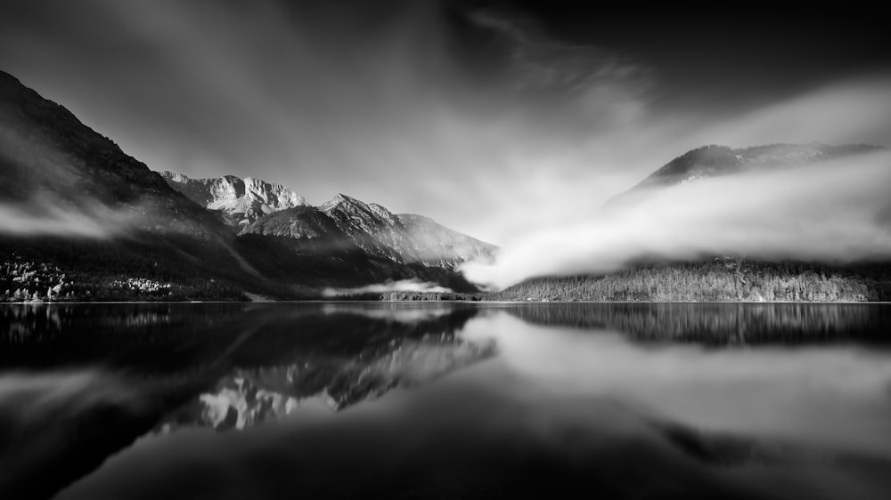 grayscale photo of snow covered mountain near body of water