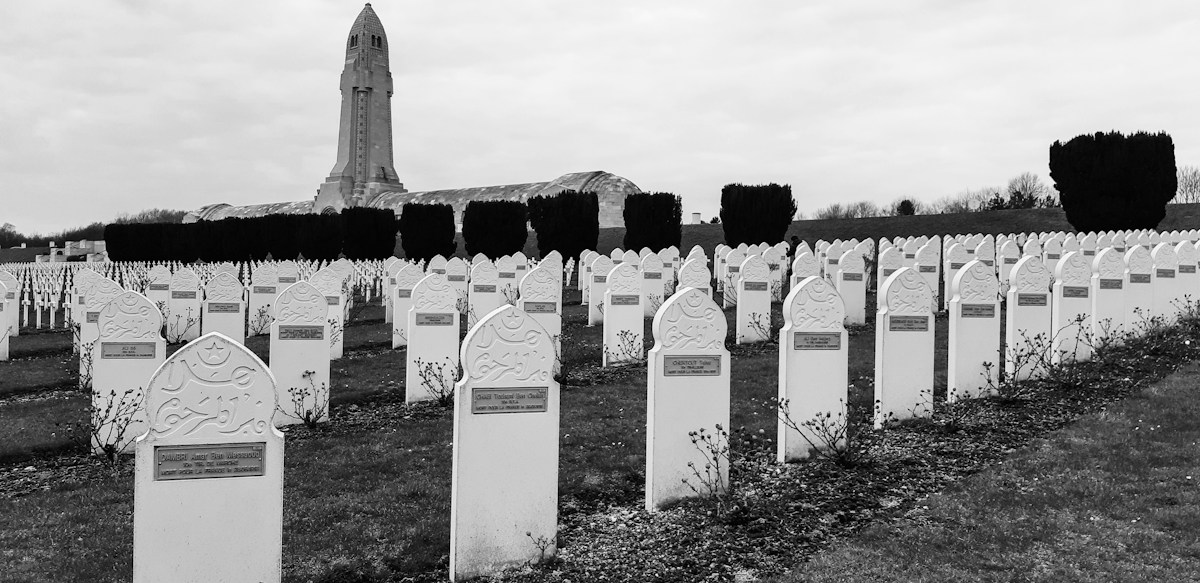 Rangées de tombes blanches dans une nécropole militaire, devant la tour d’un ossuaire, en noir et blanc