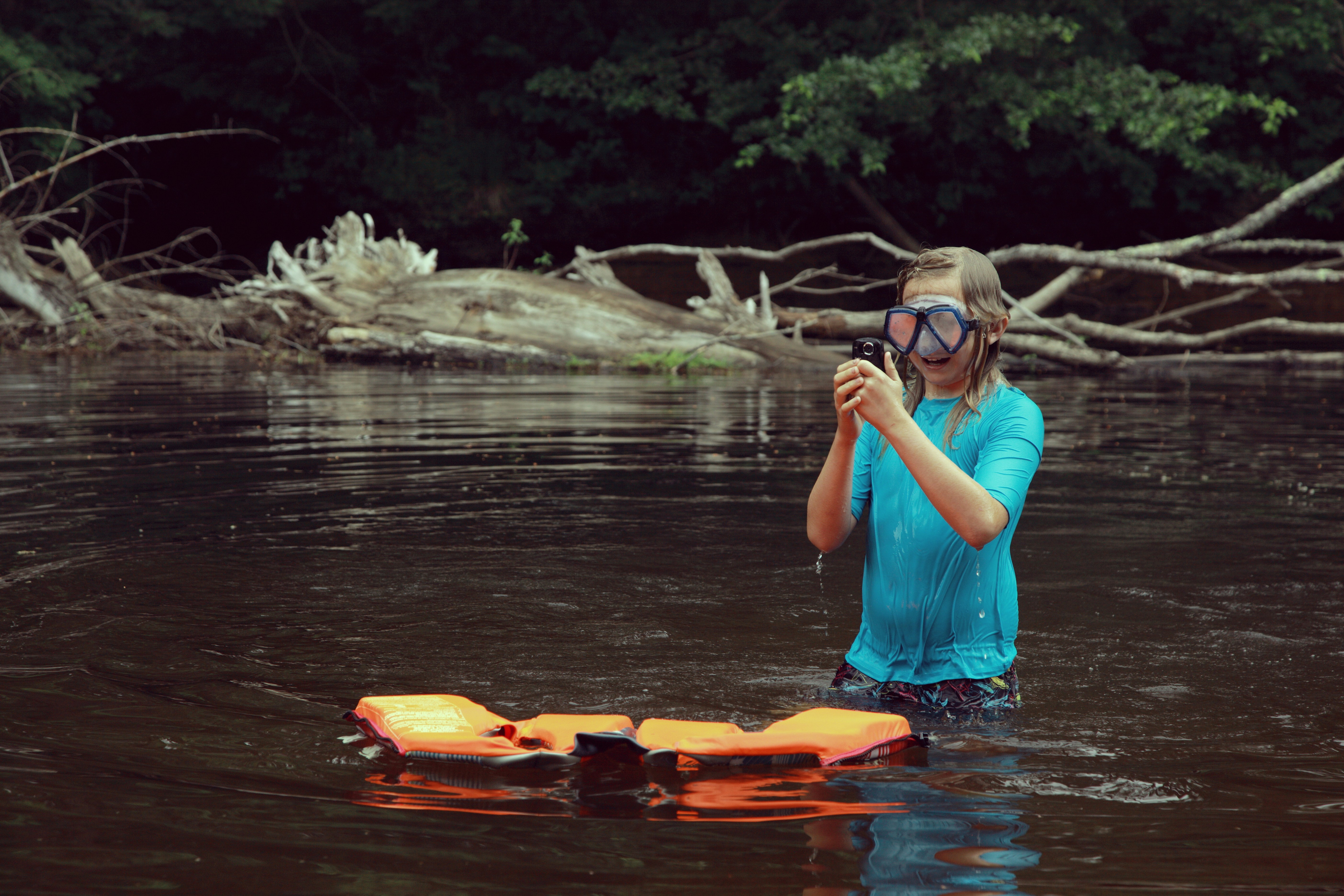 woman in blue and white polka dot tank top sitting on orange kayak on river during, My brother was taking underwater photos and video in the river. He took his life vest off, he is not a very good swimmer.  