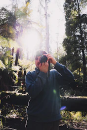 A candid shot of the photographer adjusting their camera in a sunlit forest clearing.