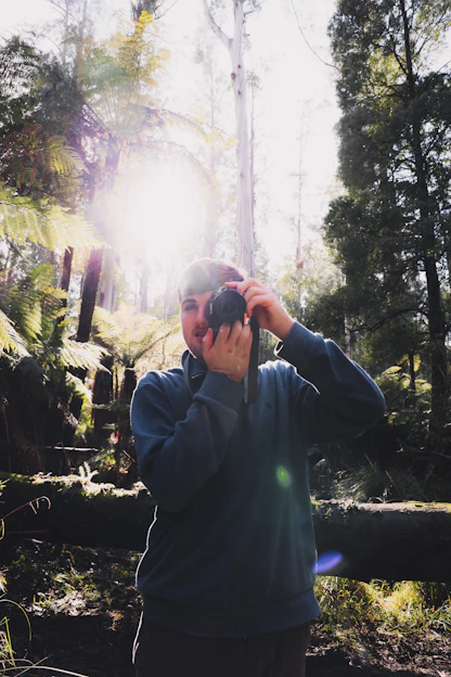 A candid shot of the photographer adjusting their camera in a sunlit forest clearing.