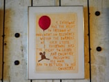 A framed poster with text that outlines the right to freedom of movement and residence within national borders. The poster is adorned with a large red balloon and an illustration of a figure holding onto the balloon string. The frame and wall have a rustic, textured appearance.