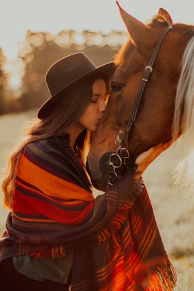 woman in black hat and brown coat beside brown horse during daytime