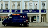 Locksmith arriving at a shopfront with a service van in a London neighborhood.