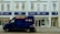 A blue security van is parked in front of a store with signage for Boots, a retail chain known for pharmacy and beauty products. The building is painted in light colors, with large windows on the upper floor. The storefront features blue signs and the Boots logo.