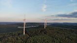 Close-up shot of wind turbines spinning gracefully on a green hill at sunrise.