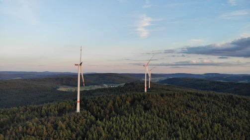 Close-up shot of wind turbines spinning gracefully on a green hill at sunrise.