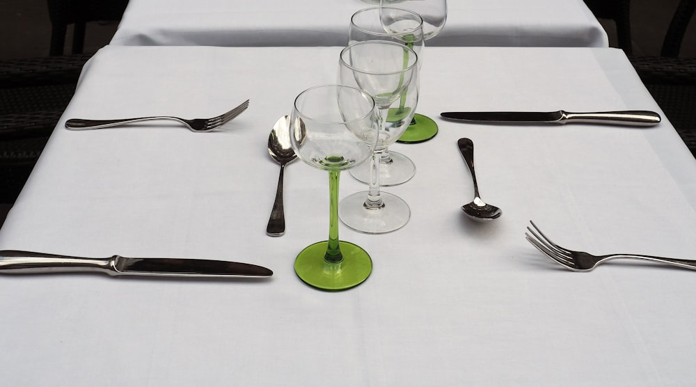 白いテーブルの上の銀のスプーンとフォークの横の透明なワイングラス