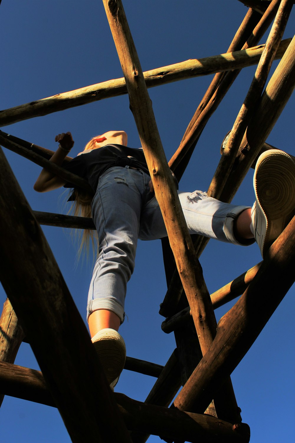 man in black t-shirt and blue denim jeans climbing on brown wooden ladder during daytime