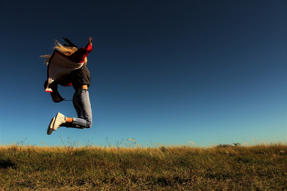 Homme en veste marron et jean bleu sautant sur un champ d’herbe verte pendant la journée