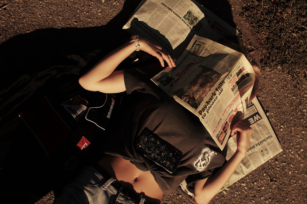 Frau in schwarzem T-Shirt und schwarzen Shorts sitzt auf dem Boden und liest Zeitung