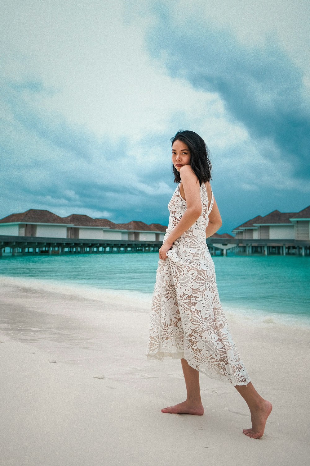 woman in white and blue floral sleeveless dress standing on beach during daytime