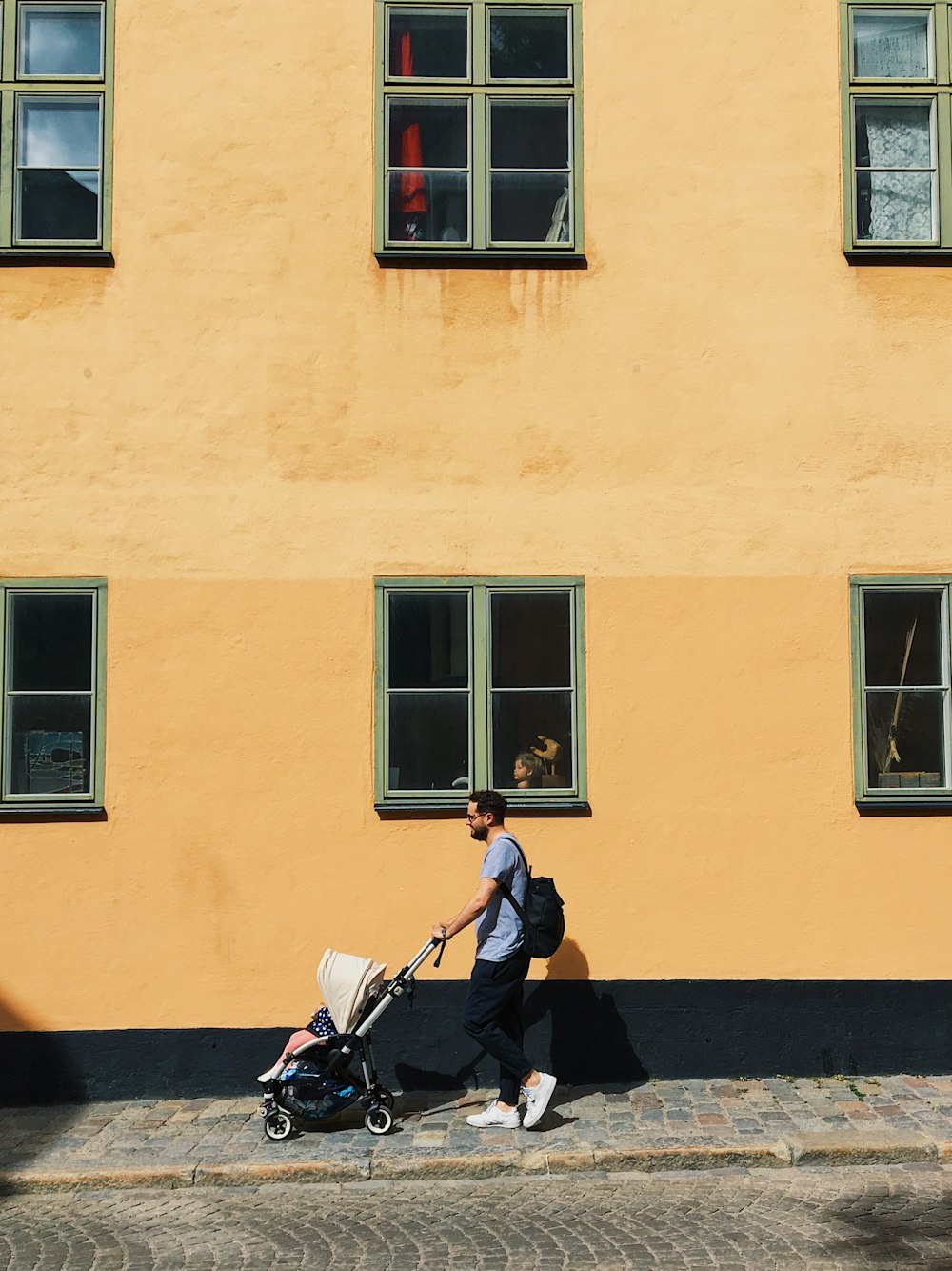 man in black suit sitting on black bench beside yellow concrete building during daytime