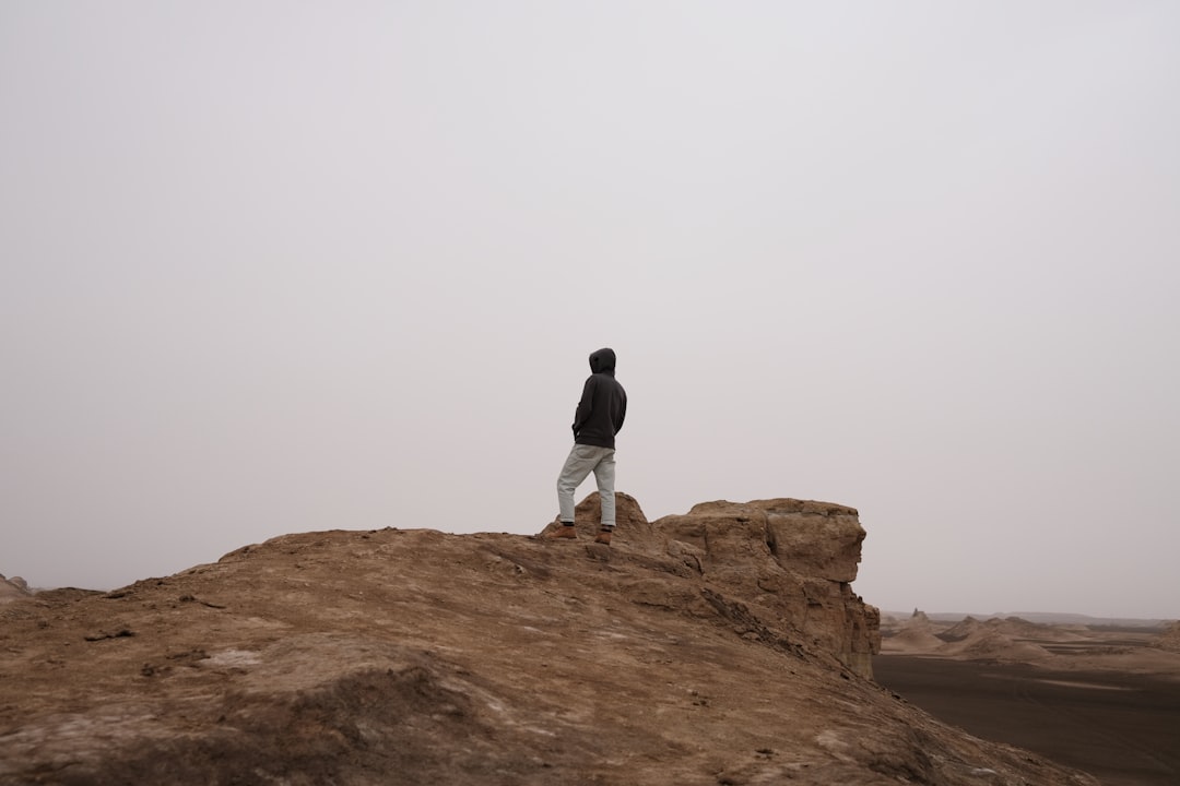 man in black jacket and white pants standing on brown rock formation during daytime