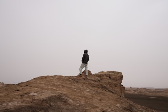 man in black jacket and white pants standing on brown rock formation during daytime in Qinghai China