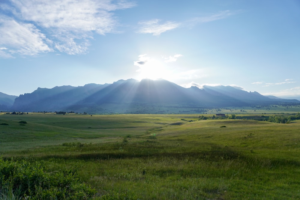 green grass field near mountain under white clouds during daytime