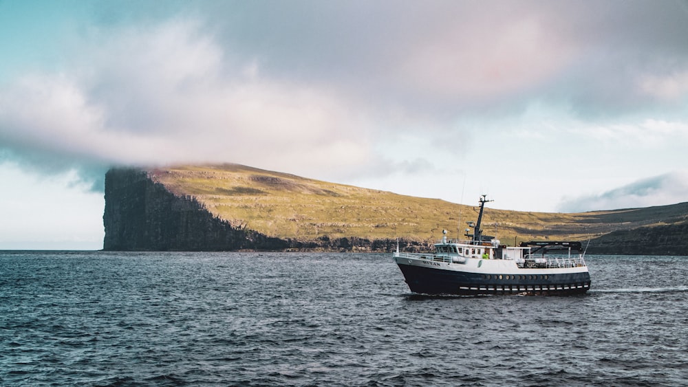 white and black ship on sea near brown mountain under white clouds during daytime