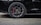 A close-up view of a sleek black car's wheel, featuring a detailed alloy wheel design and red brake calipers.