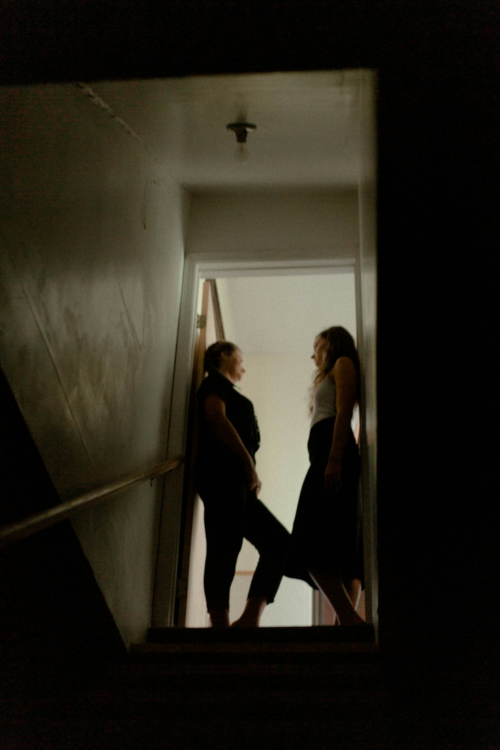 白い廊下に立つ黒いタンクトップと黒いズボンの女性