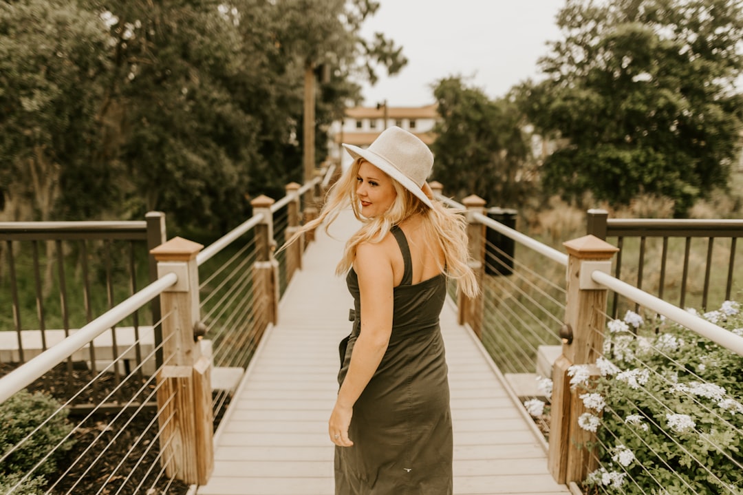 woman in black spaghetti strap dress and brown hat standing on wooden bridge during daytime