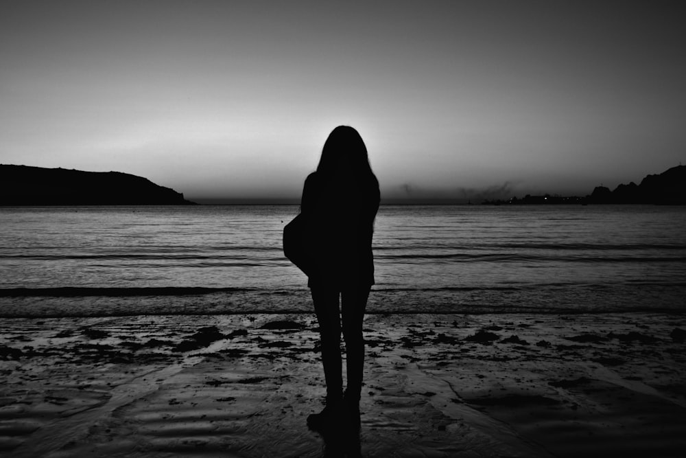 silhouette di donna in piedi sulla spiaggia durante il giorno