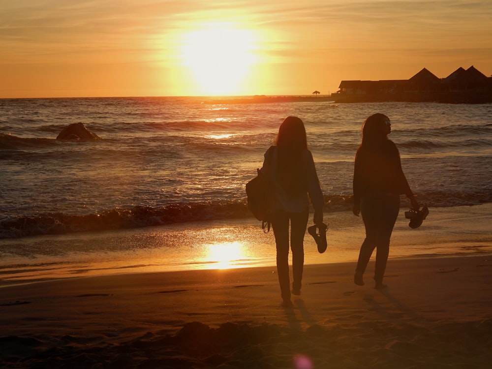 silhueta de 2 mulheres que caminham na praia durante o pôr do sol