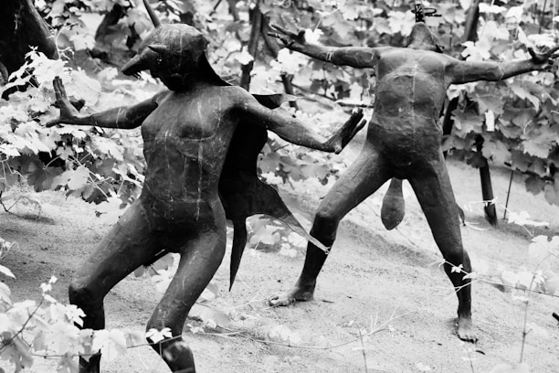 Sculptures of humanoid figures resembling mythological creatures with animalistic features are posed dynamically among a backdrop of leafy vines. The figures appear to be made of a dark material and are set in various dramatic stances.