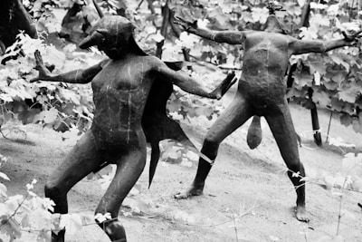 Sculptures of humanoid figures resembling mythological creatures with animalistic features are posed dynamically among a backdrop of leafy vines. The figures appear to be made of a dark material and are set in various dramatic stances.