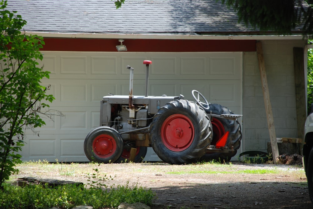 Tractor rojo estacionado al lado de una casa de madera blanca durante el día