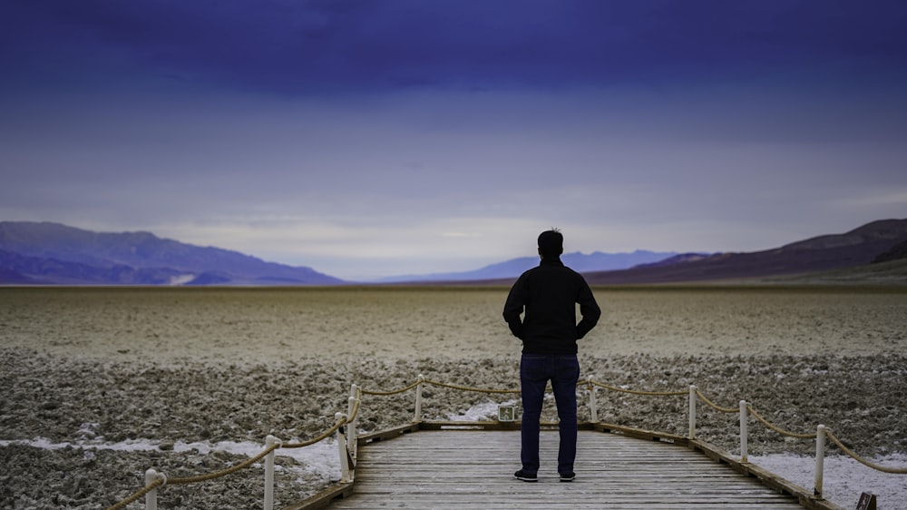 man in black jacket standing on wooden dock during daytime