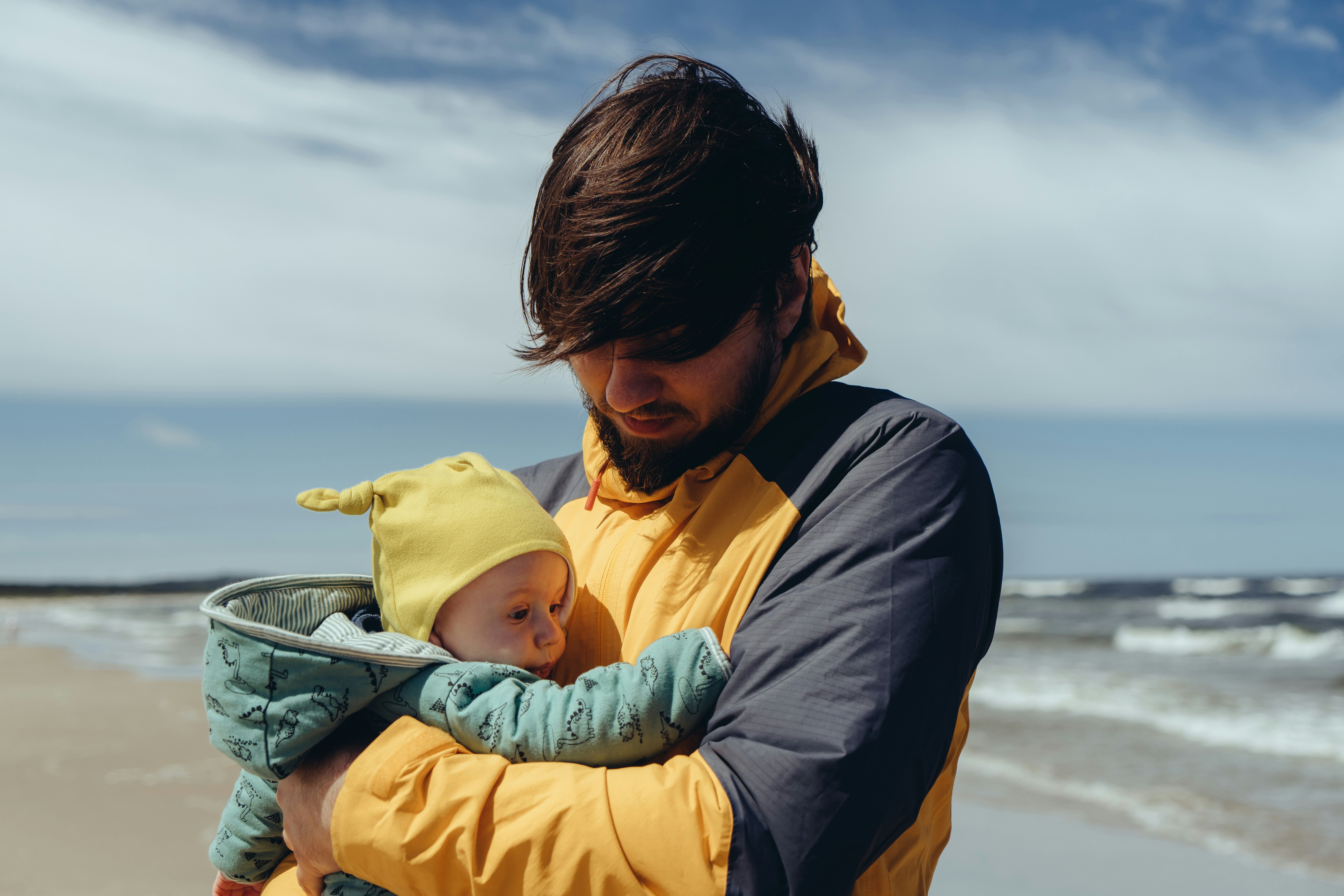 man in black jacket carrying baby in yellow hoodie