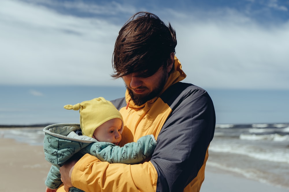 Foto hombre con chaqueta negra cargando bebé con capucha amarilla – Imagen  Bebé gratis en Unsplash