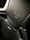 A close-up view of a sleek, black car seat with intricate stitching and a luxurious texture. An embossed logo featuring a shield and crown is prominently displayed on the upper section. The seat has perforated leather sections for ventilation and integrated grip holes on the sides, suggesting it is designed for high-performance or sport vehicles.