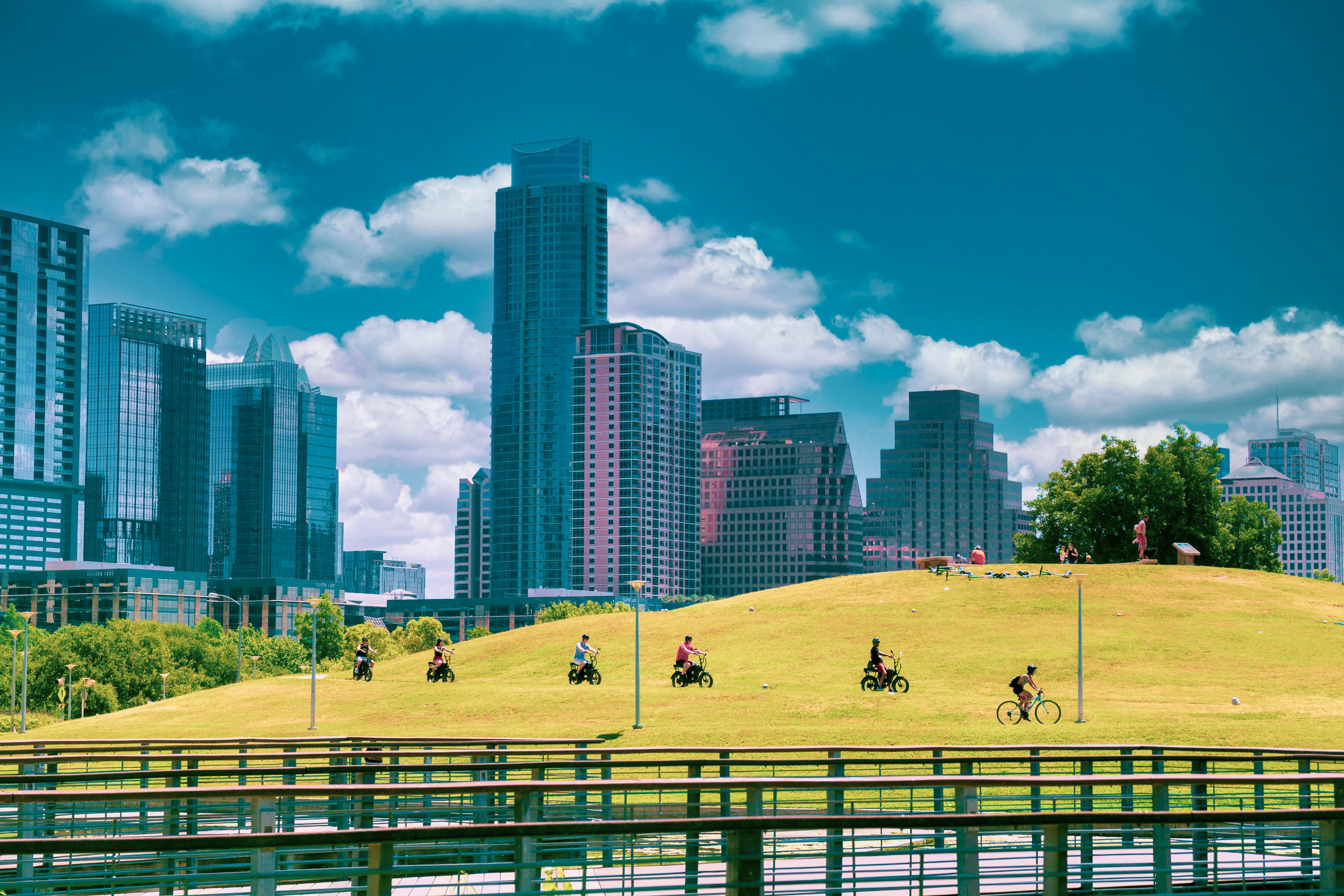people playing on green grass field near city buildings under blue and white sunny cloudy sky