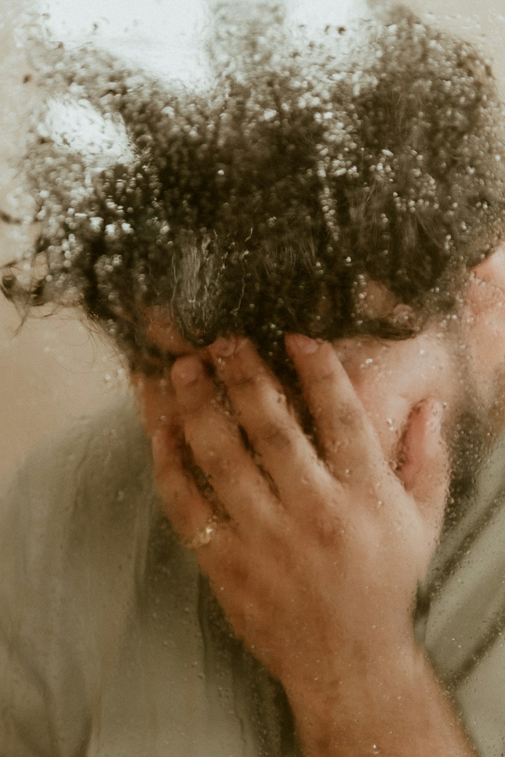 man in gray shirt covering his face