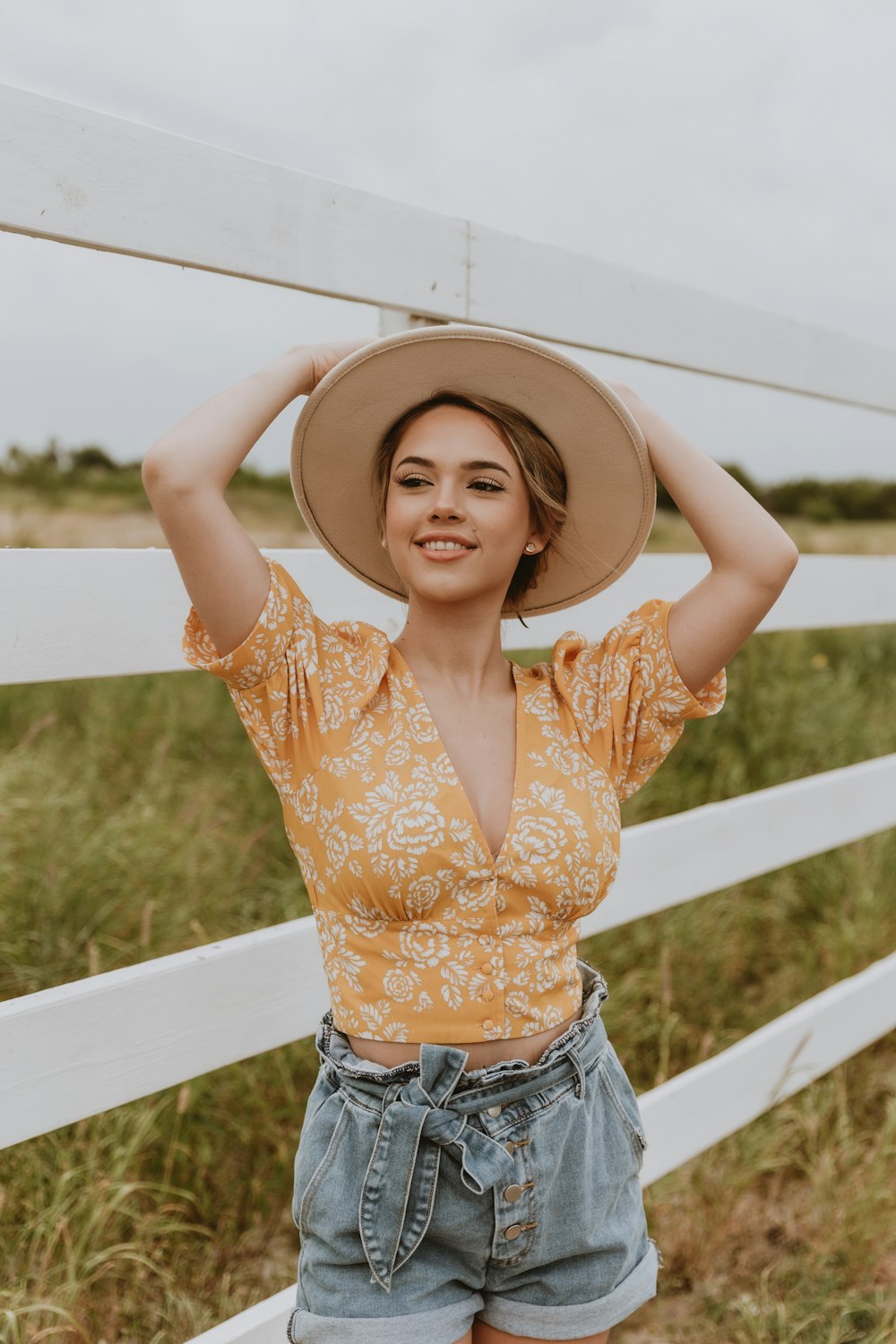 woman in orange and white floral crop top and blue denim daisy dukes wearing brown sun