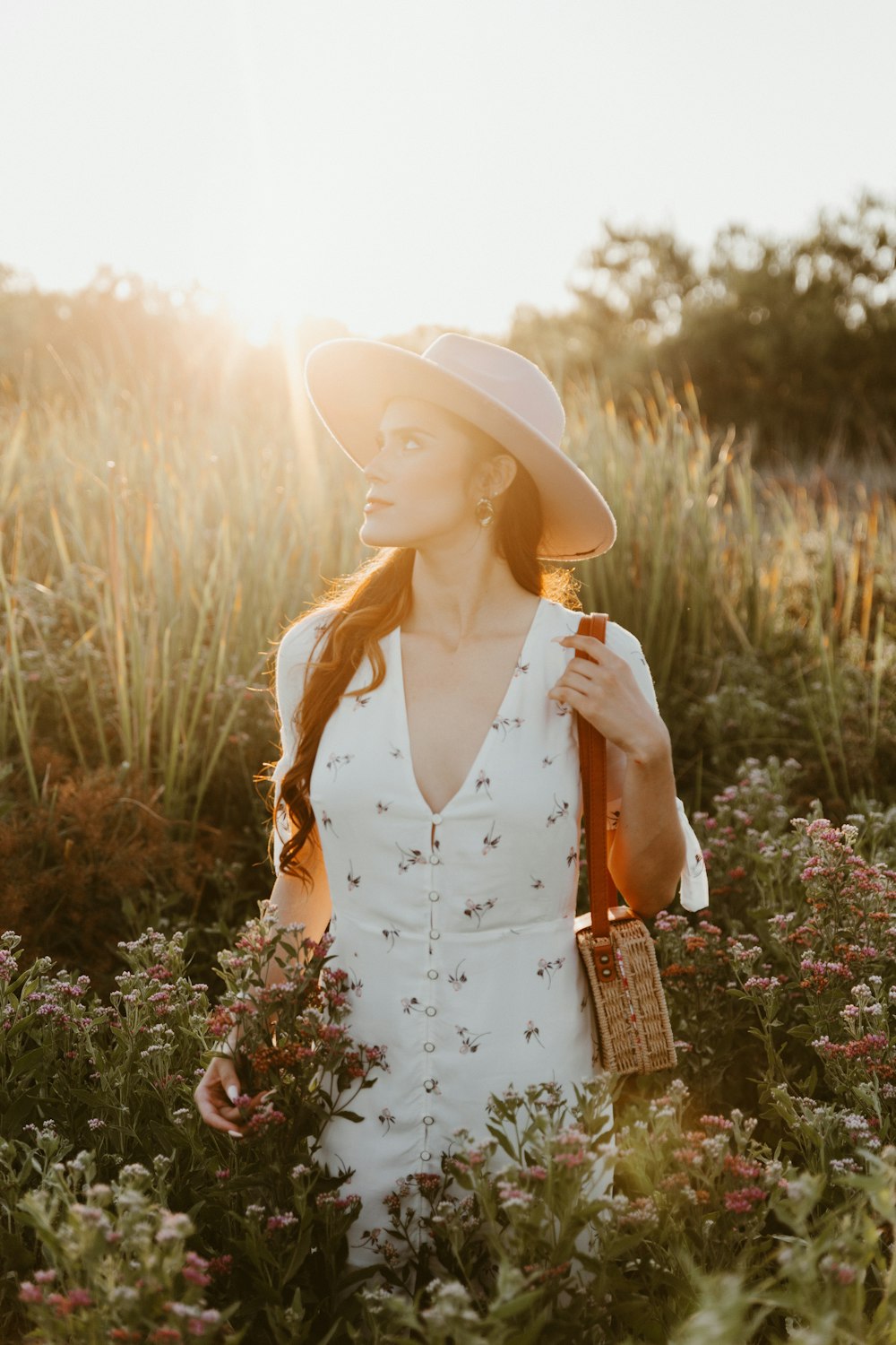 woman in white and black floral sleeveless dress wearing white sun hat standing on green grass