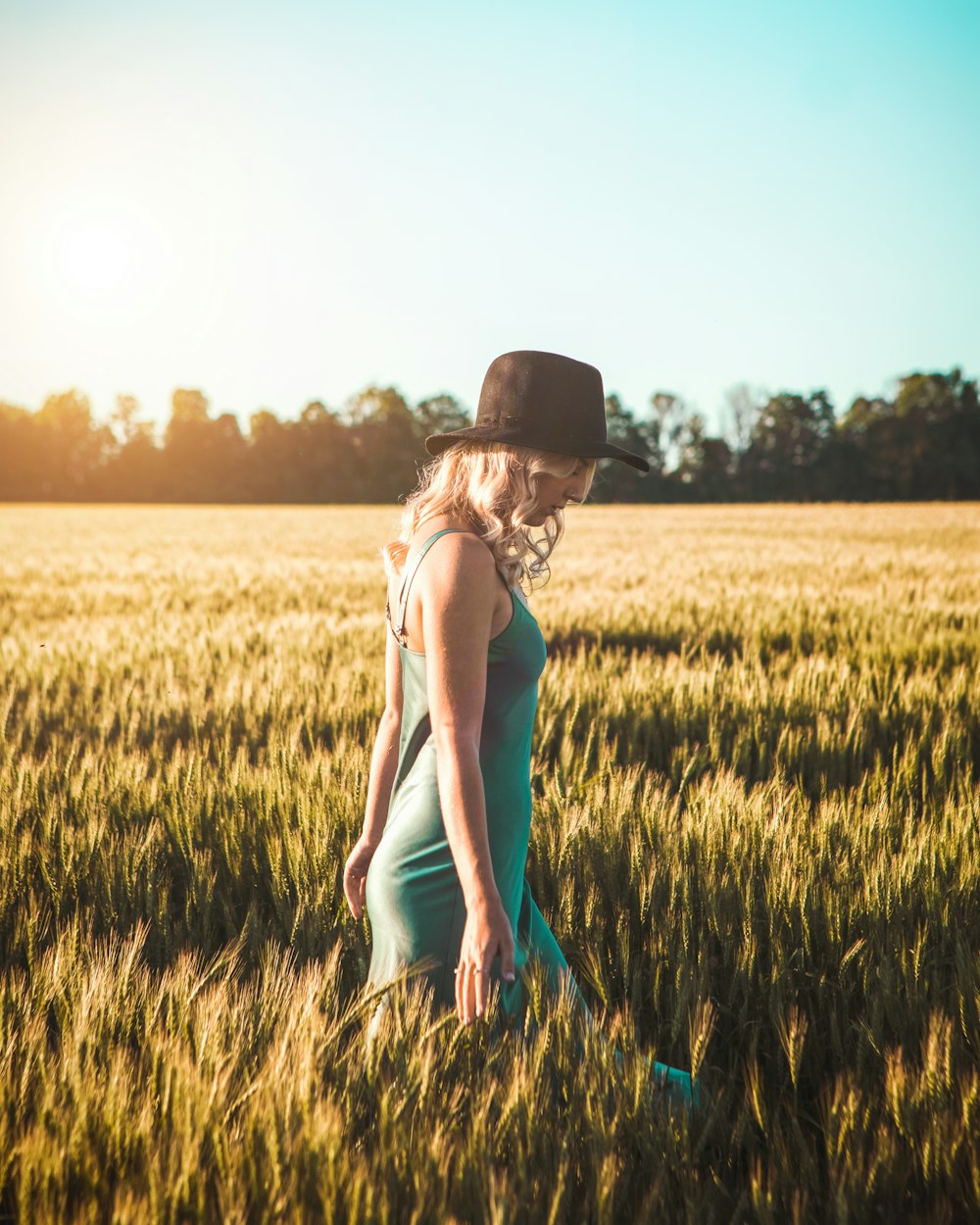 woman in white tank top and black fedora hat standing on green grass field during daytime