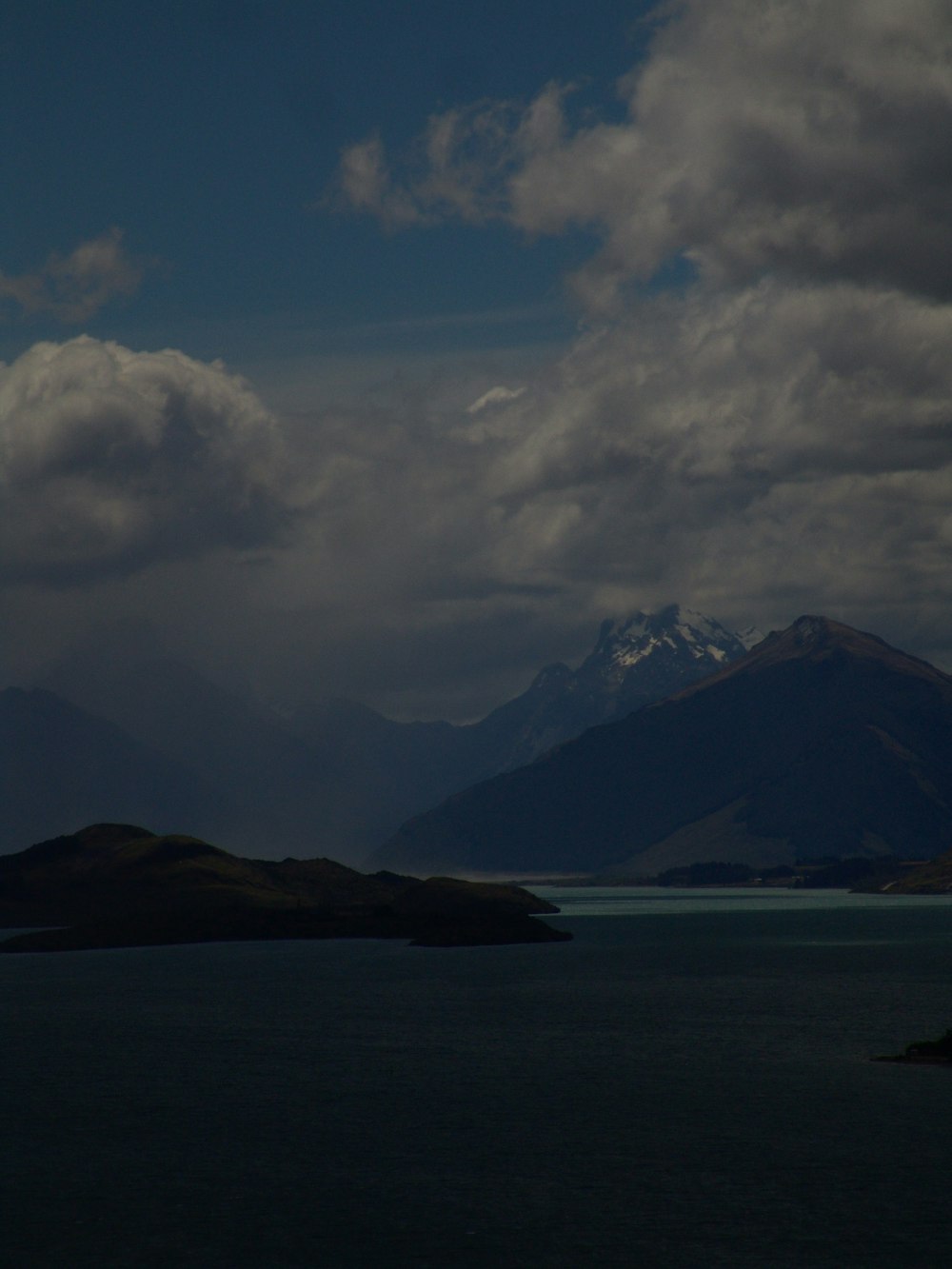 body of water near mountain under white clouds during daytime