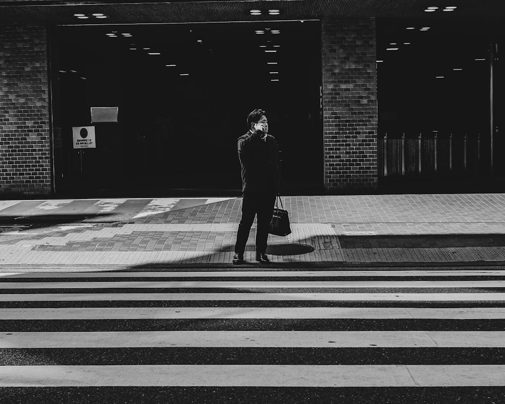 grayscale photo of man walking on pedestrian lane