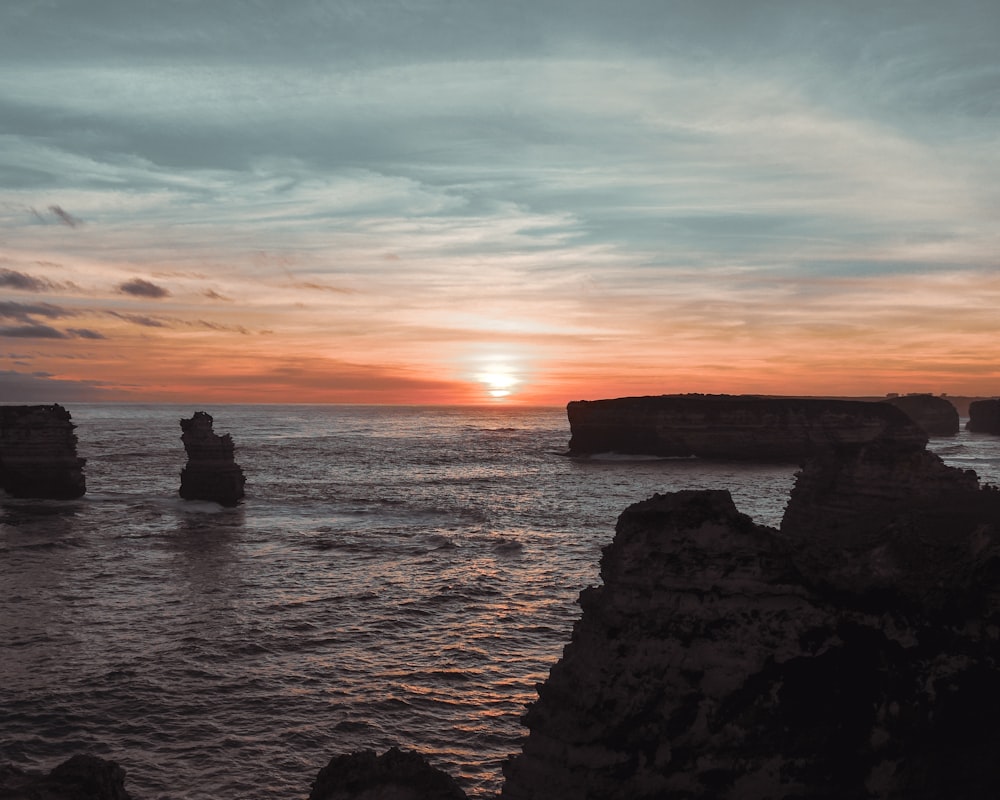 silhouette of 2 people sitting on rock formation near sea during sunset