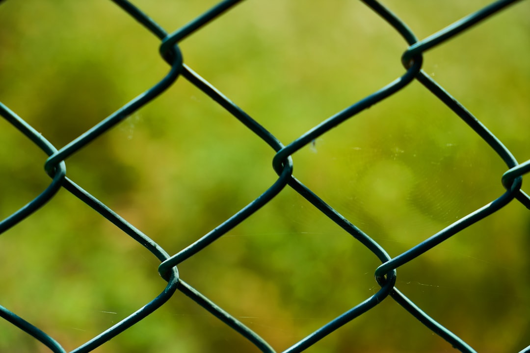 grey metal fence with green grass field in background during daytime