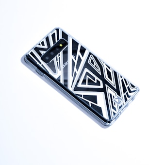 A smartphone encased in a geometric patterned case, positioned diagonally on a bright white surface. The back camera and branding are visible, adding a sleek and modern aesthetic.