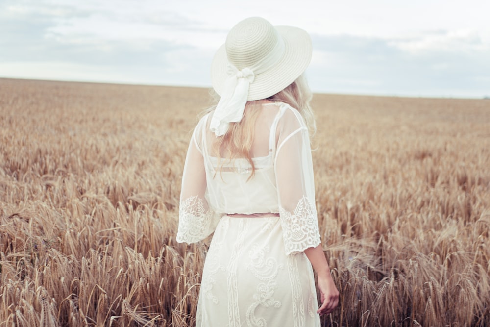 woman in white dress wearing white sun hat standing on brown grass field during daytime