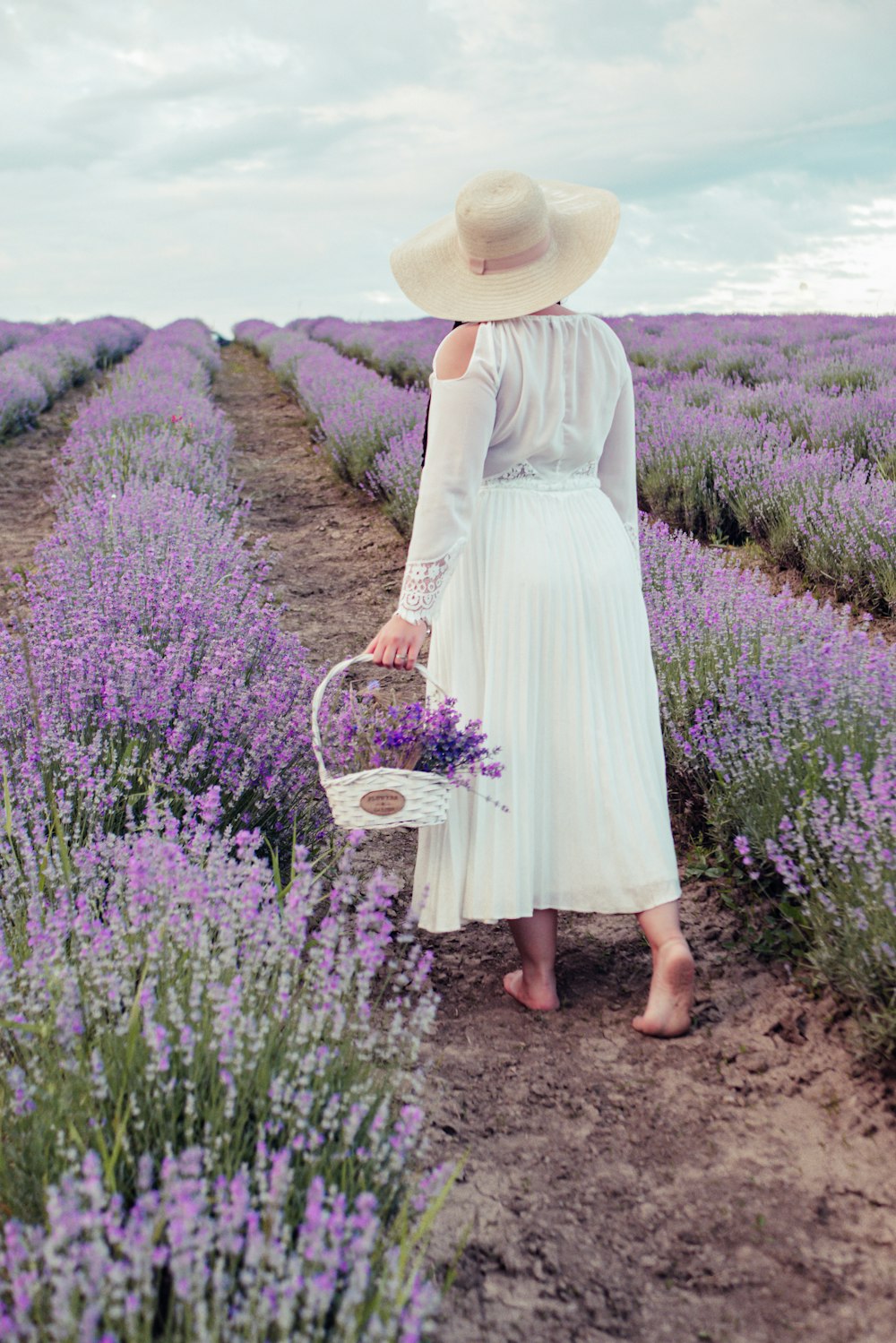 woman in white dress holding basket walking on purple flower field during daytime