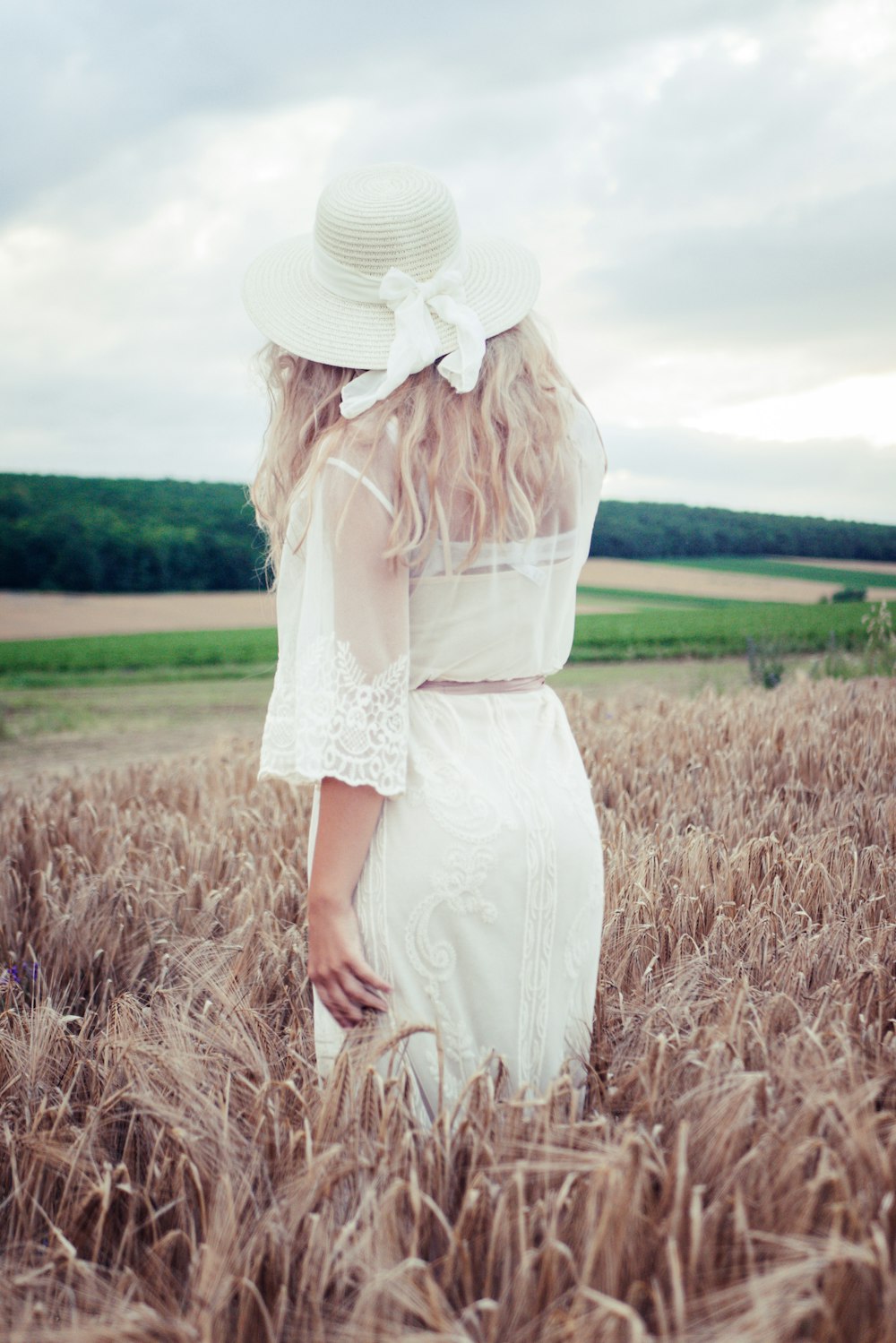 Mujer en vestido blanco de pie en el campo de hierba marrón durante el día