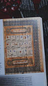 A page featuring intricate Islamic calligraphy enclosed in decorative borders with floral and geometric patterns. The artwork is richly detailed and set against a textured background, showcasing a blend of artistic and religious expression.