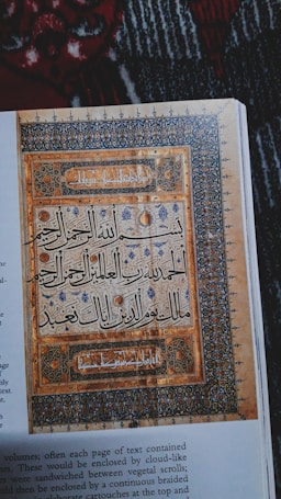 A page featuring intricate Islamic calligraphy enclosed in decorative borders with floral and geometric patterns. The artwork is richly detailed and set against a textured background, showcasing a blend of artistic and religious expression.